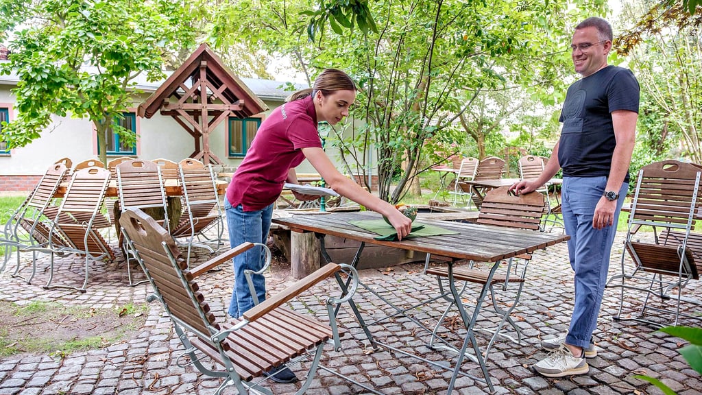 Inhaber Frieder Jage und Kellnerin Julia decken den Tisch im gemütlichen Biergarten für Mittagsgäste ein.