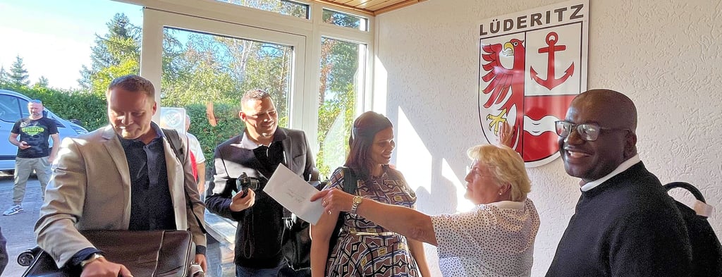 Edith Braun (2. von rechts) erklärt den Gästen aus Namibia Wappen und Ehrungen des Dorfes Lüderitz im Eingangsbereich der Mehrzweckhalle. Von rechts: Verwaltungschef Otto Shipanga, Anne-Marie Hartzenberg, Randel Beukes und Phillipus A. Balhao.