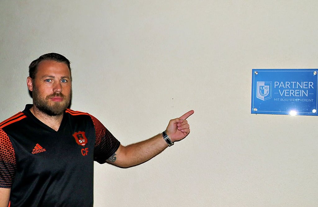 Christian Feger zeigt auf das Partnervereins-Schild des 1. FC Magdeburg.