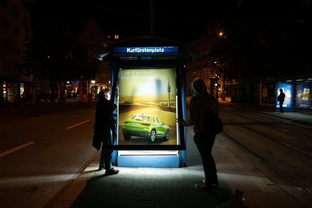 Aktivisten von Attac bringen als Protest gegen die IAA kritische Persiflagen von Autowerbung an einem Trambahnhäuschen an.