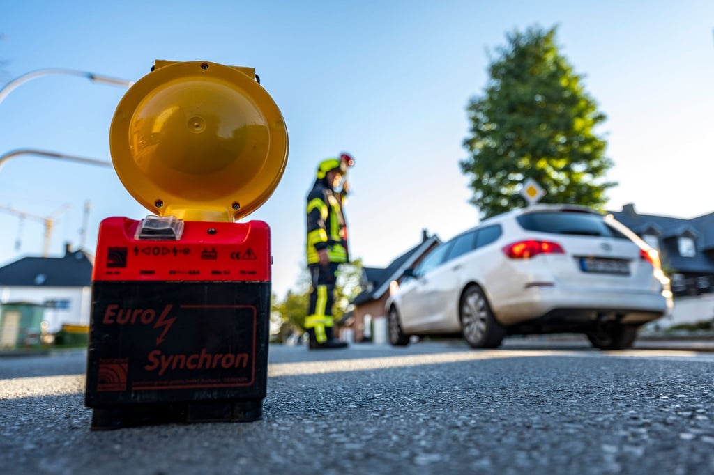 Ein Feuerwehrmann hat eine Straßensperre errichtet und leitet den Verkehr um den Einsatzort herum.