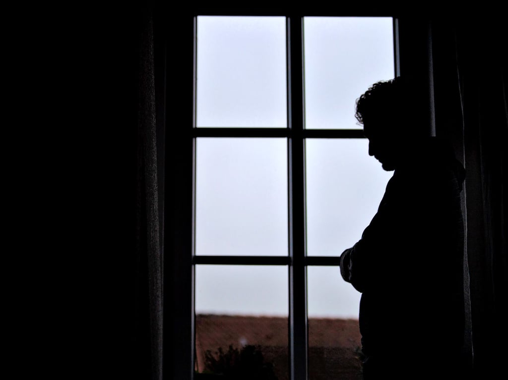 Ein Mann steht am Fenster seiner Wohnung (gestellte Szene). Einsamkeit ist ein Thema, das immer mehr Menschen betrifft. Ein junger Mann erzählt, was sie mit ihm gemacht hat.