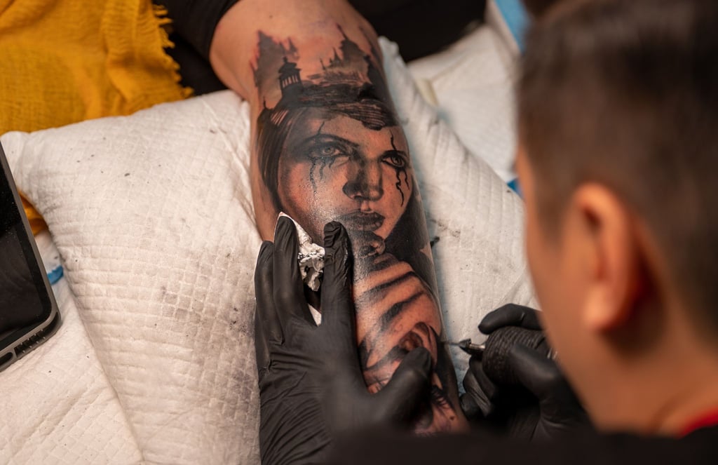 Ein Tätowierer sticht auf der 30. Internationalen Tattoo Convention (2022) ein Tattoo auf dem Bein einer Besucherin.
