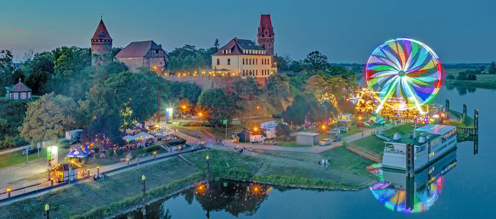 Blick auf das Burgfest 2023 am Hafen am Freitagabend mit Hafen-Schänke (von links), Hotel Schloss Tangermünde auf der Burg Tangermünde, Riesenrad und Restaurantschiff „Störtebeker“.