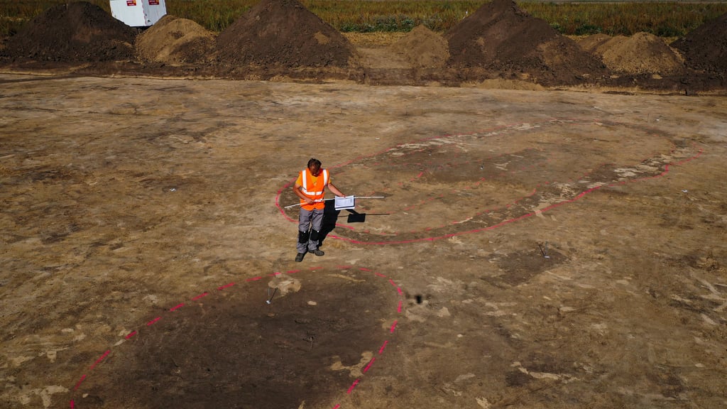 Der Archäologe Nikita Sirman vom Landesamt für Denkmalpflege und Archäologie vermisst und kartiert den mutmasslichen Grundriss eines Grubenhauses, während dahinter der Grundriss eines zehn Meter langen und vier Meter breiten Hauses zu sehen ist (Aufnahme mit Drohne)