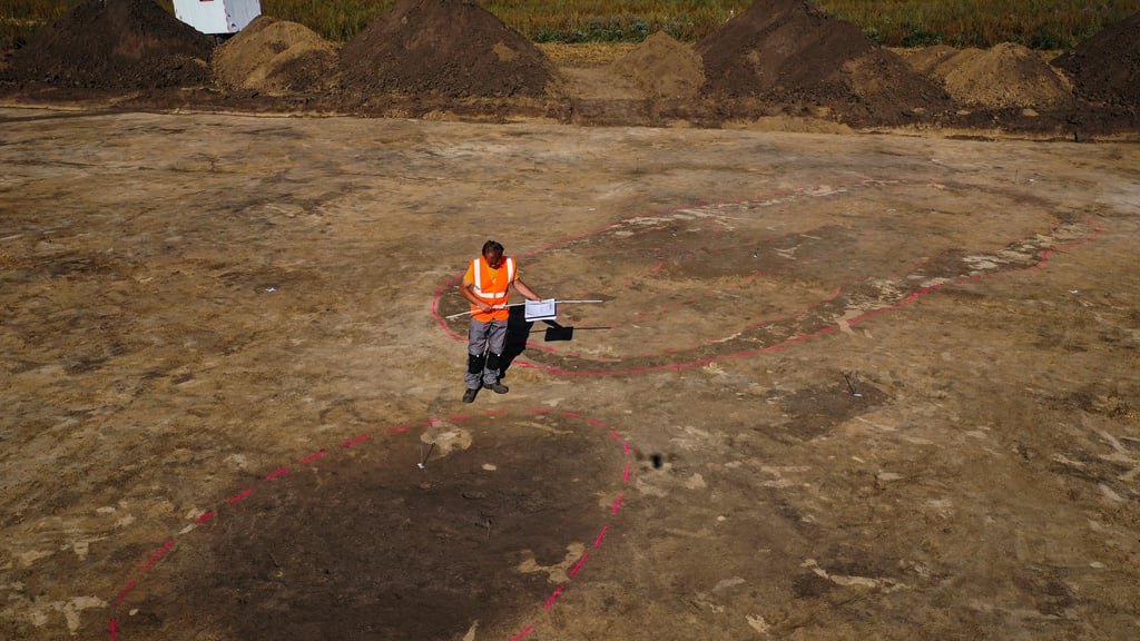 Der Archäologe Nikita Sirman vom Landesamt für Denkmalpflege und Archäologie vermisst und kartiert den mutmasslichen Grundriss eines Grubenhauses, während dahinter der Grundriss eines zehn Meter langen und vier Meter breiten Hauses zu sehen ist (Aufnahme mit Drohne)