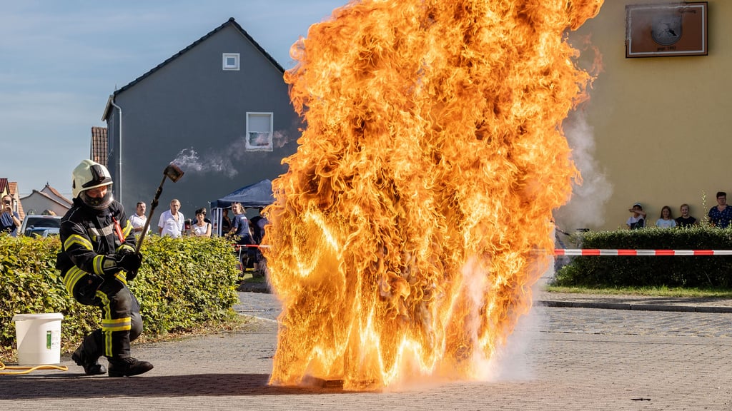 Pascal Obst (l.) zeigt in Annaburg die Folgen, wenn brennendes Fett mit Wasser gelöscht wird: Zuerst sinkt das Wasser im Topf unter das leichtere Öl. Dann verdampft es. Der aufsteigende Wasserdampf verdrängt das Öl – einen Großteil zerstiebt es nach oben, ein Teil läuft brennend über.