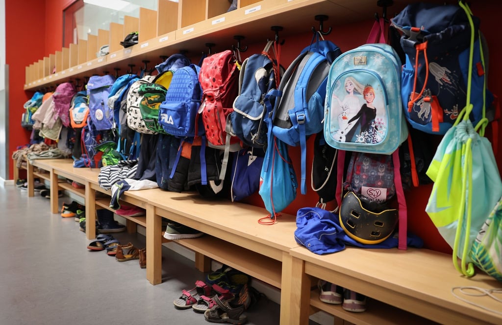 Sporttaschen und Schulranzen hängen an der Garderobe vor einem Klassenzimmer.