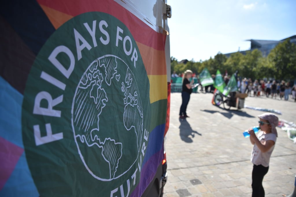 Eine Regenbogenfahne mit Logo von Fridays for Future hängt an der Rückseite eines kleinen Transportwagens.