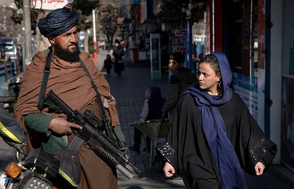 Ein Taliban-Kämpfer steht in Kabul Wache, während eine Frau vorbeiläuft. (Archivbild)