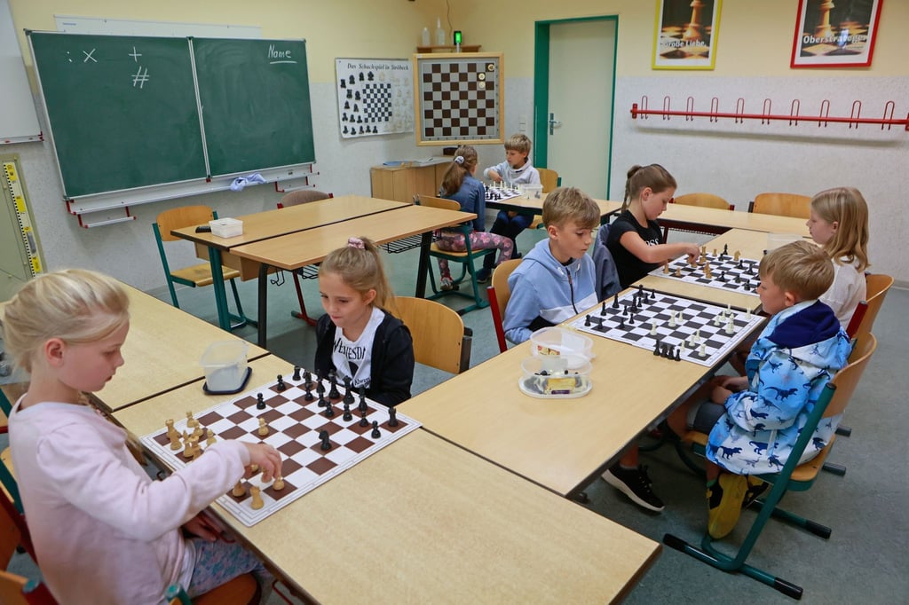 Schulkinder sitzen im Klassenraum und spielen Schach.
