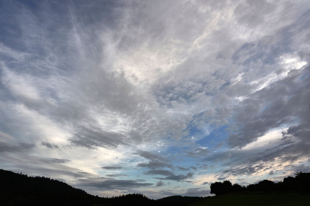 Eine aufreißende Wolkendecke zieht über eine Wiese hinweg.