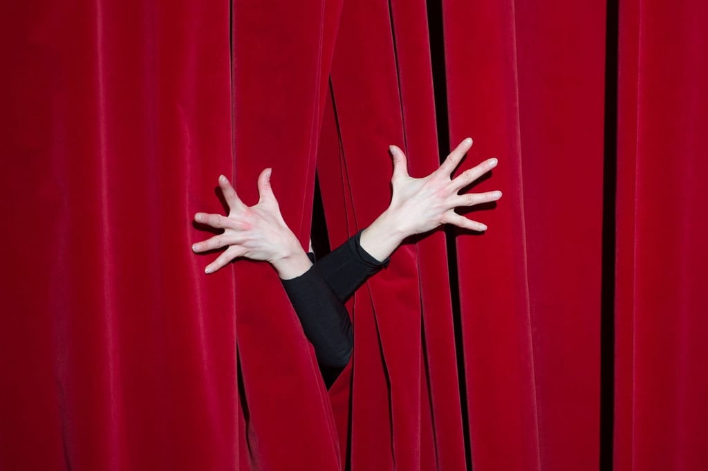 Die Hände einer Schauspielerin auf einem roten Vorhang.