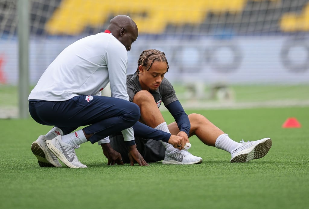 Leipzigs Spieler Xavi Simons zieht sich die Schuhe an, neben ihm Babacar N'Diaye, Teammanager.