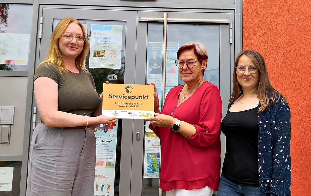 Gudrun Speldrich (M.) vom Servicepunkt Nachbarschaftshilfe nimmt das Schild von Sarah Poppe (l.) und Stefanie Hamacher entgegen.