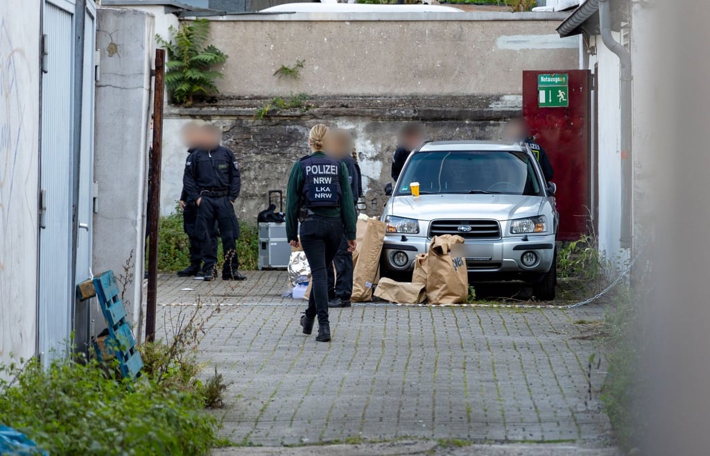 Polizistinnen und Polizisten stehen in einem Hinterhof in der Duisburger Innenstadt, auf dem Boden stehen Papiertüten mit Beweismitteln.