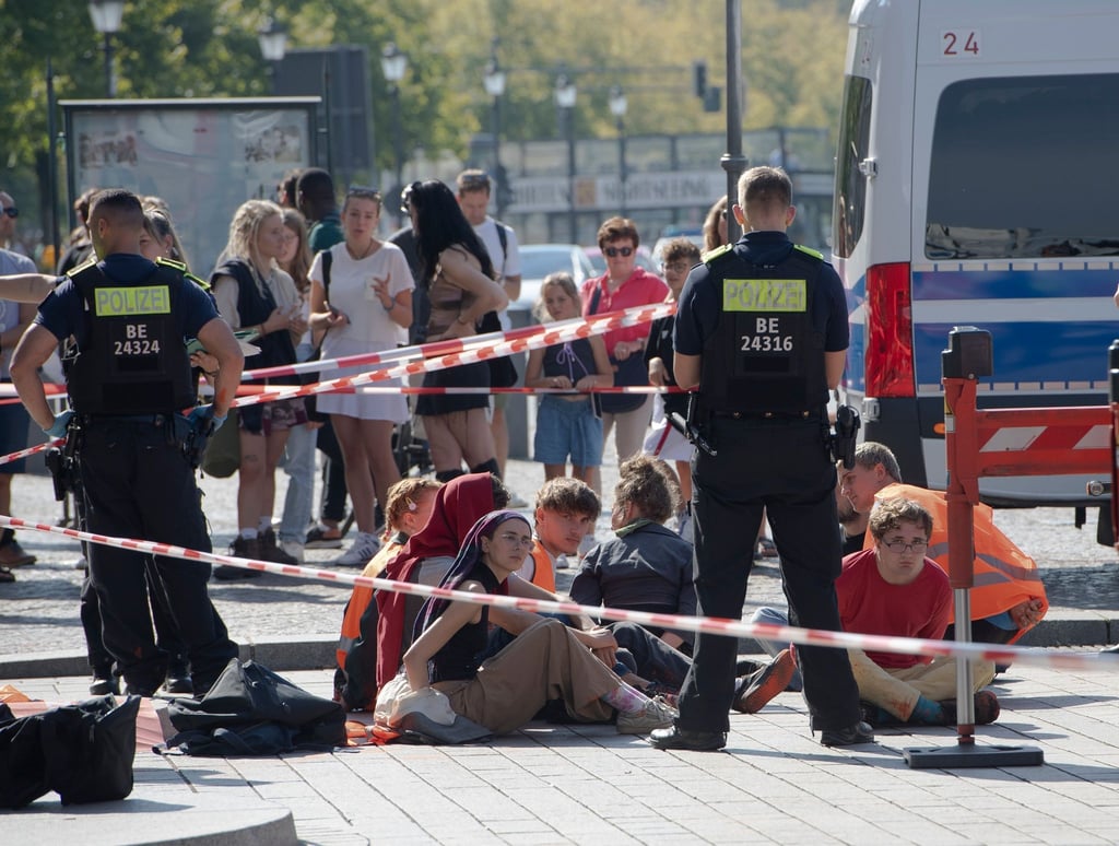 Polizeibeamte stehen um eine Gruppe festgesetzter Mitglieder der Klimaschutzgruppe Letzte Generation.