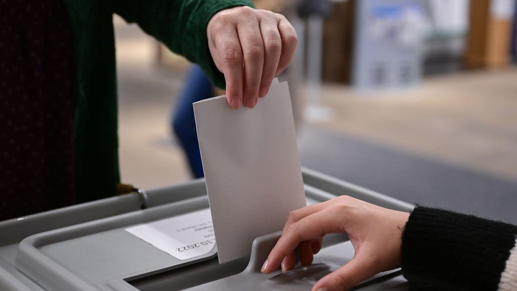 Ein Wähler steckt bei einer Wahl seinen Wahlzettel in eine Urne.