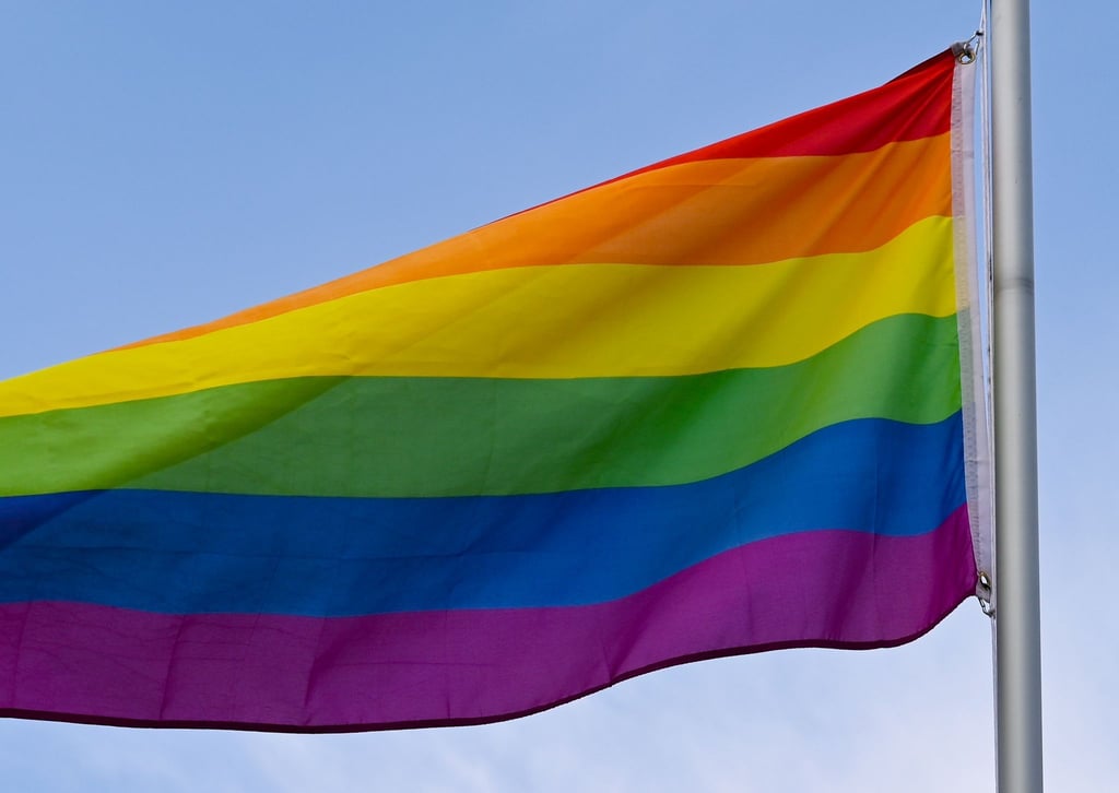 Die Regenbogenfahne weht vor dem blauen Himmel.