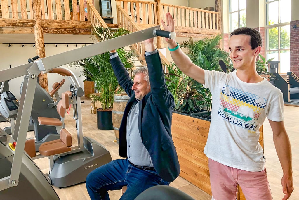 Müchelns Bürgermeister Andreas Marggraf probiert im neuen Fitnessstudio von Tobias Moses (rechts) die Schulterpresse aus.