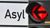 Eine rote Ampel leuchtet vor dem Wort „Asyl“ auf einem Wegweiser zur Erstaufnahme-Einrichtungen (EAE).