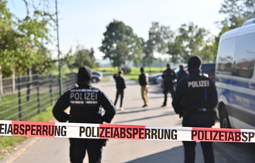 Einsatzkräfte der Polizei stehen hinter einer Polizeiabsperrung nach einer Razzia in Hesselbronn.