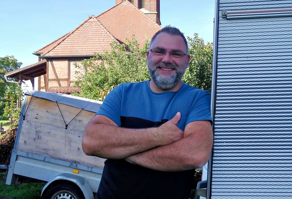 Bürgermeisterkandidat Kevin Schröter wohnt neben der Kirche in Aulosen (Altmark). Hier lehnt er an seinem Wohnwagen, mit dem seine Familie schon manche Trips an die Ostsee unternahm.