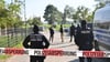 Einsatzkräfte der Polizei stehen hinter einer Polizeiabsperrung nach einer Razzia in Hesselbronn.
