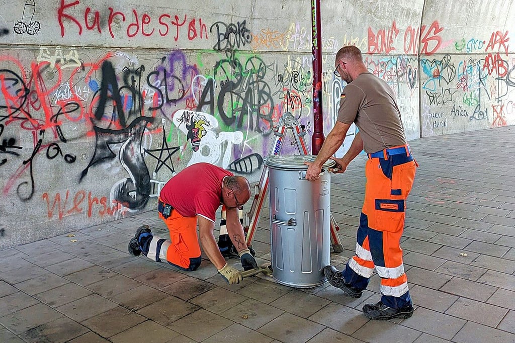 Frank Reimer (l.) und Daniel Schäl von der Stadtwirtschaft stellen in dem Fußgängertunnel einen Müllkübel für leere Farbdosen auf.