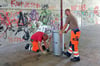 Frank Reimer (l.) und Daniel Schäl von der Stadtwirtschaft stellen in dem Fußgängertunnel einen Müllkübel für leere Farbdosen auf. 