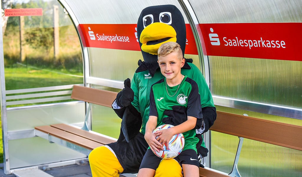 Maskottchen Rudi und der neunjährige Bastian auf einer der neuen Spielerbänke auf Platz zwei