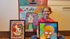 Amy Licht mit zwei von ihr gemalten Bildern und der Spülmaschine in der Küche (im Hintergrund), die die Elfjährige aus Hohenmölsen mit einem Bild versehen hat.