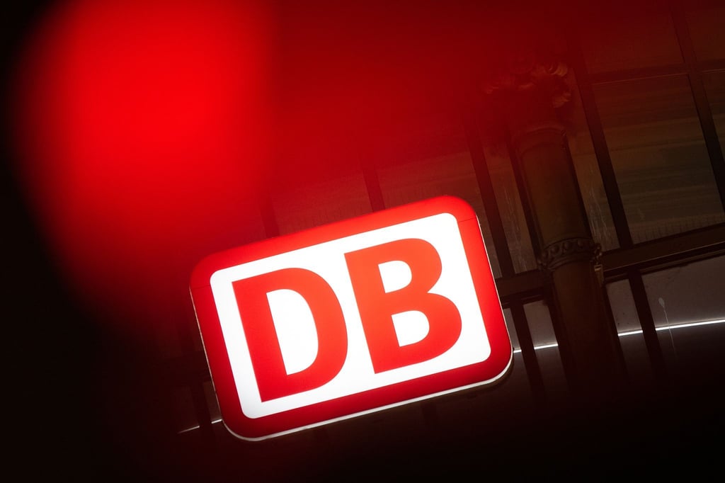 Das Logo der Deutschen Bahn leuchtet an einem Bahnhof hinter einer Ampel.