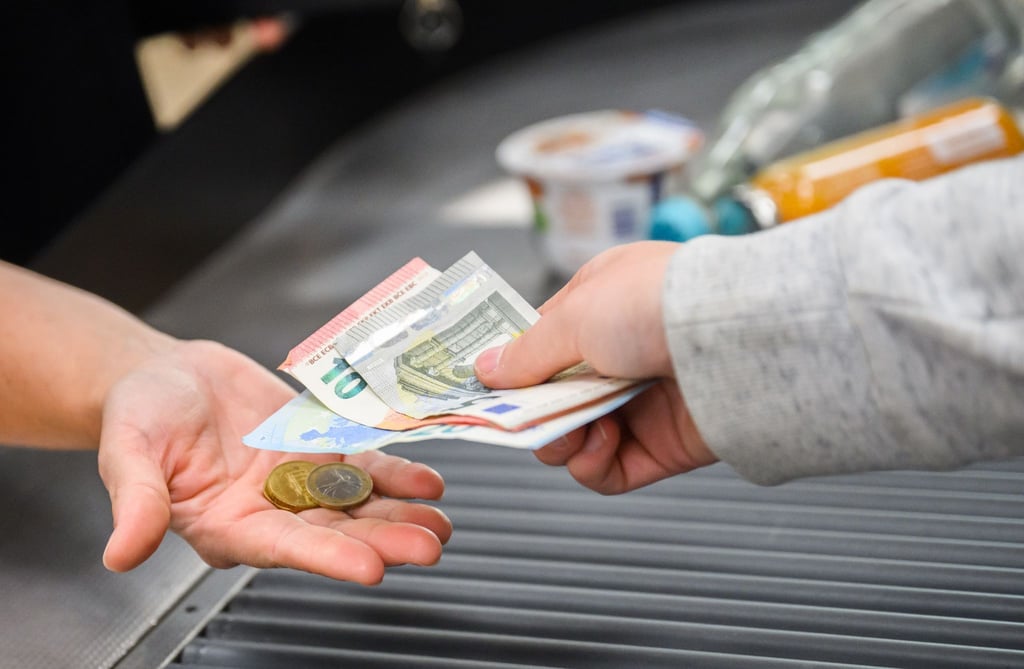 Eine Kassiererin reicht einer Kundin Wechselgeld an der Kasse eines Supermarkts.