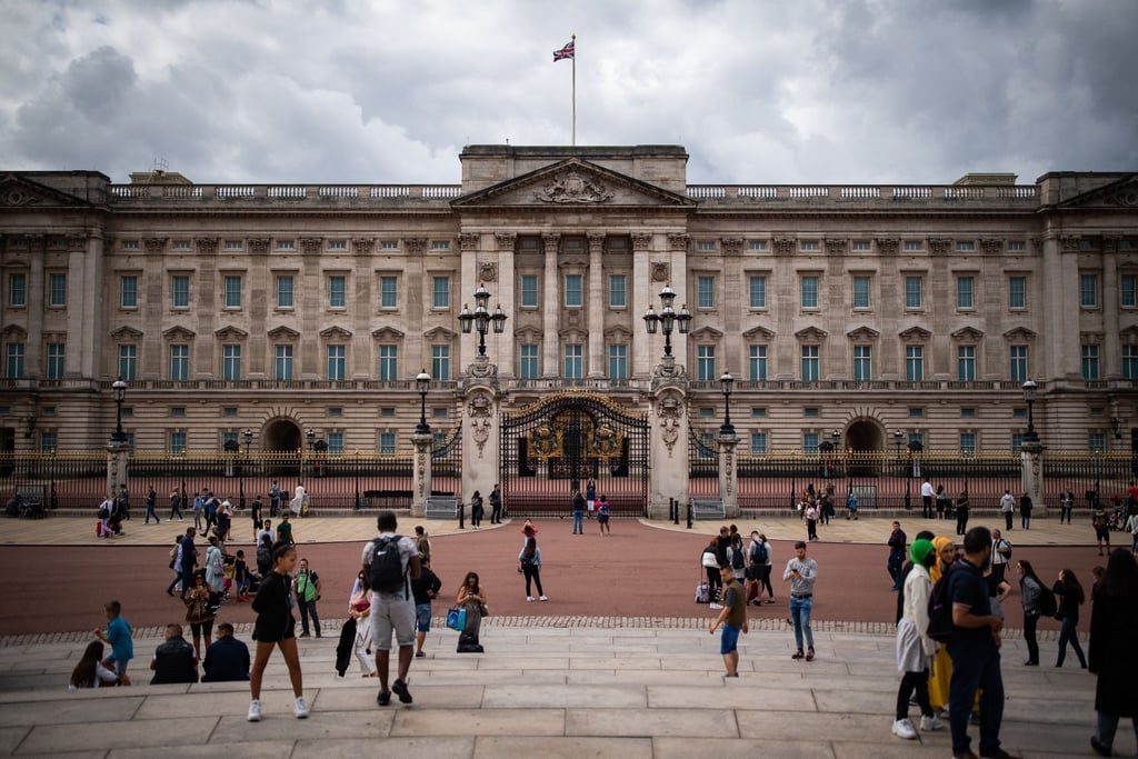 Touristen stehen vor den Toren vom Buckingham Palast in London.
