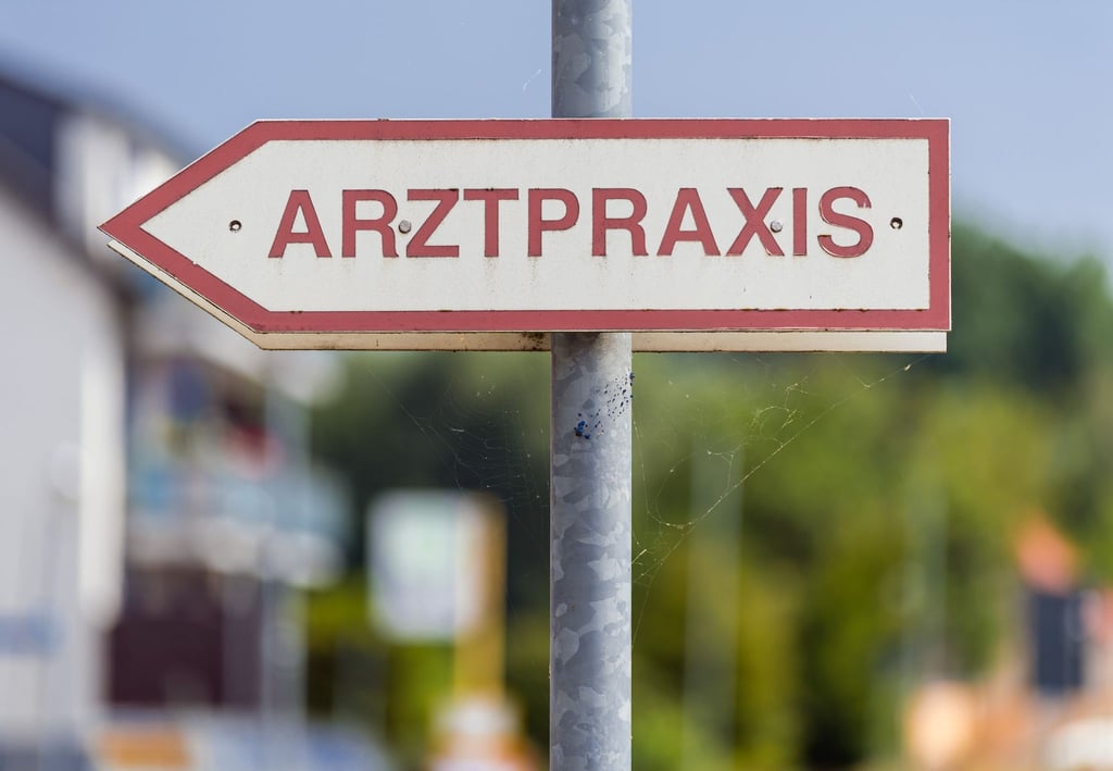 Ein Schild „Arztpraxis“ steht an der Straße.