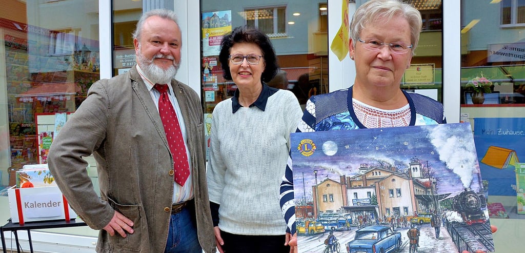 Rosemarie Kiehne (r.) und Sabine Kühne vom Lions Club Oschersleben präsentieren den Adventskalender. Das Motiv wurde von Kay Elzner (l.) gezeichnet.