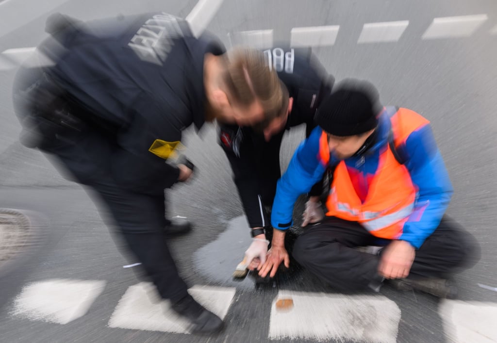 Polizisten versuchen die festgeklebte Hand eines Aktivisten von der Straße zu lösen.