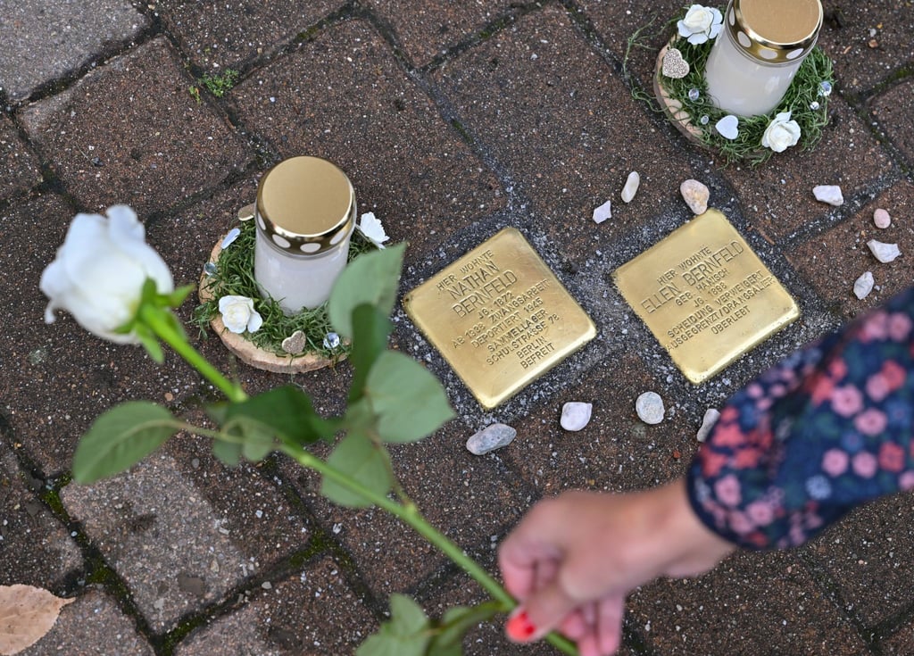 Eine Frau legt eine weiße Rose neben zwei der frisch verlegten Stolpersteine in Spremberg.
