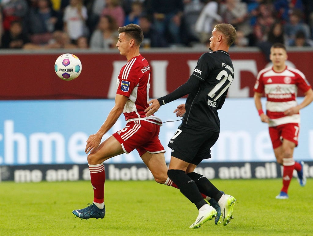 Düsseldorfs Yannik Engelhardt (l) und der Osnabrücks Michael Bruno Cuisance kämpfen um den Ball, während die Fans in der ersten Hälfte schweigen.