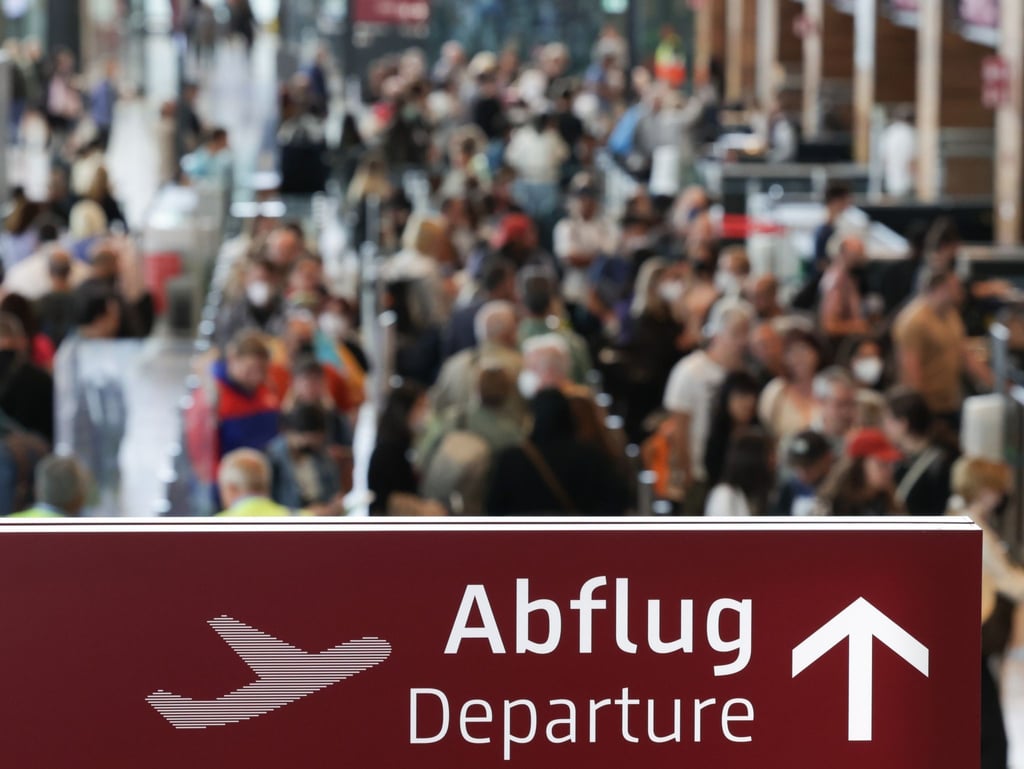 Am Flughafen Berlin Brandenburg BER stehen zahlreiche Reisende in einer Schlange.