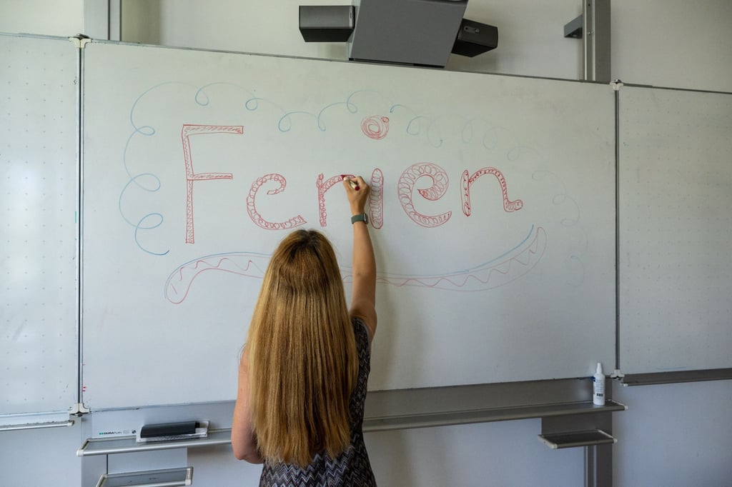Eine Lehrerin schreibt das Wort „Ferien“ an die Klassentafel.