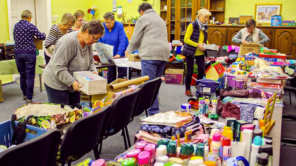 Freiwillige der Volkssolidarität packen mit Spenden Weihnachtspäcken für Kinder.