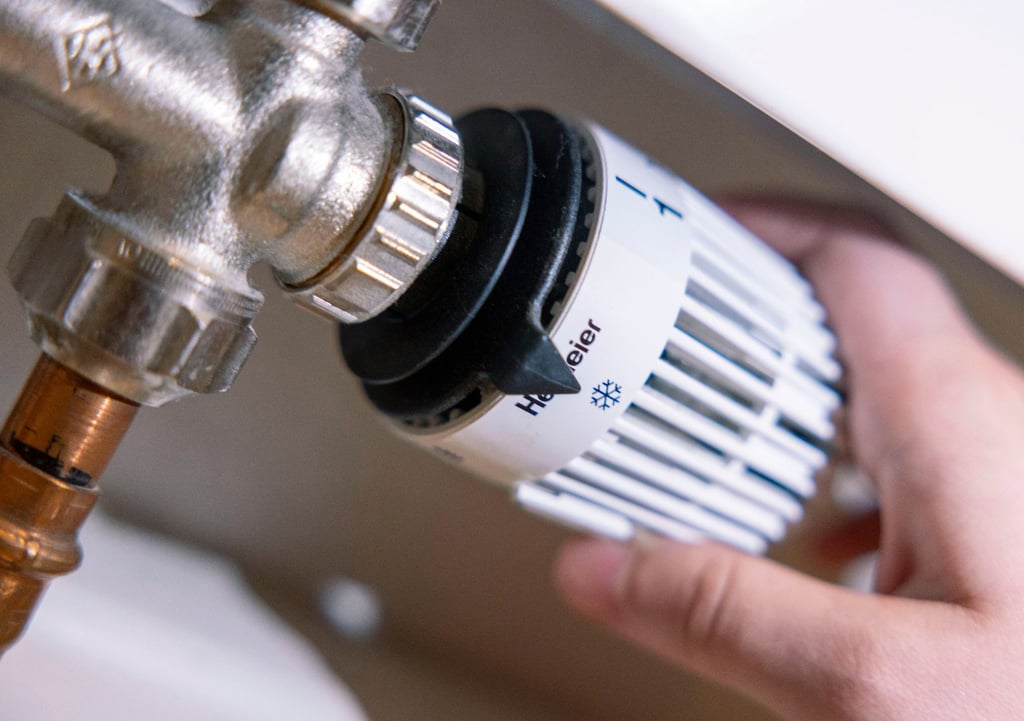 Eine Person dreht am Thermostat einer Heizung.