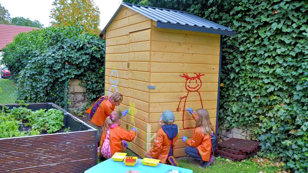 Haily (6, Bahrendorf, links), Lio, Maria und Amy (6, Dodendorf, rechts) beginnen mit dem Malen der Frühlingslandschaft auf dem Gartenhäuschen.