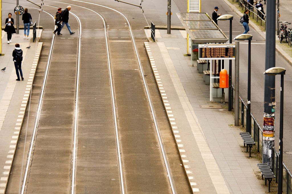 Menschen stehen an der Haltestelle einer Straßenenbahn in Berlin.