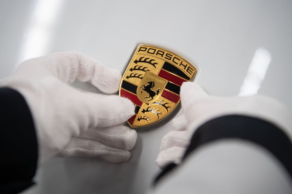Eine Mitarbeiterin der Porsche AG hält in der Produktion ein Porsche-Emblem auf die Motorhaube eines Porsche Taycan.