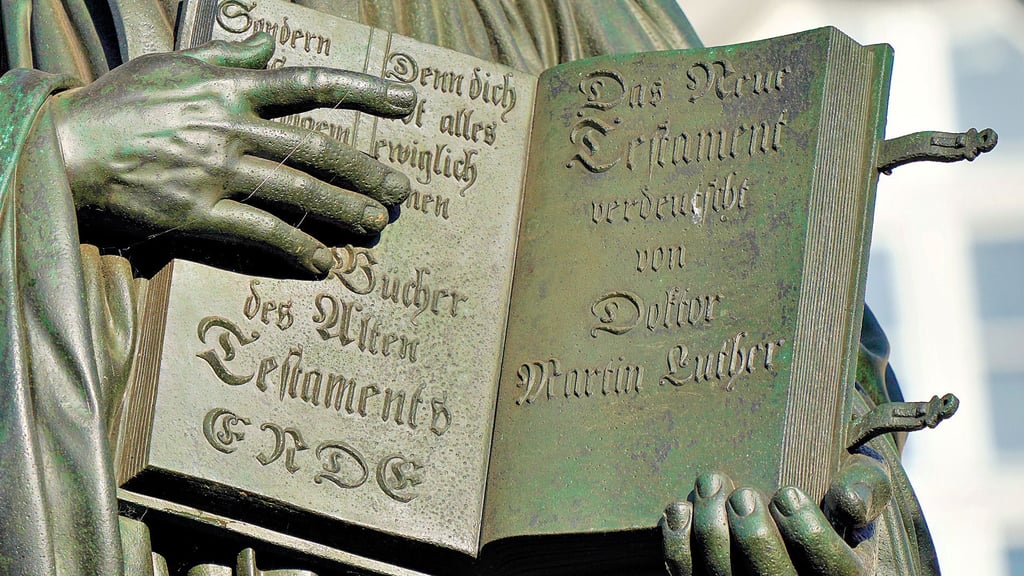 Das übersetzte Neue Testament hält der Reformator in dem Lutherdenkmal in Wittenberg.
