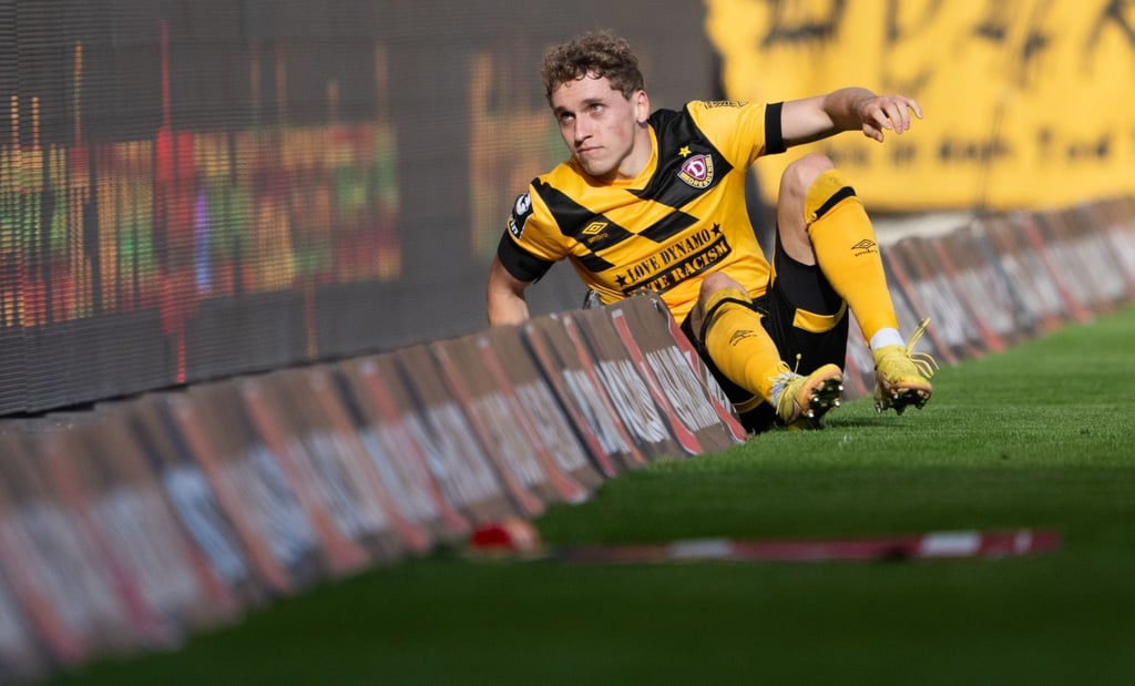 Dynamos Luca Herrmann sitzt in der Bandenwerbung. In Saarbrücken rutschten er und seine Mitspieler öfter über den Rasen.