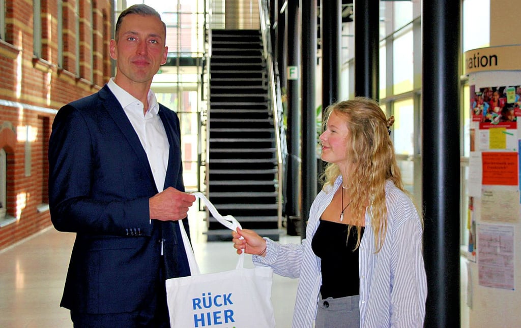 Stendals Oberbürgermeister Bastian Sieler übergibt in der Wandelhalle des Stadthauses den ersten Beutel an eine zugezogene Studentin.